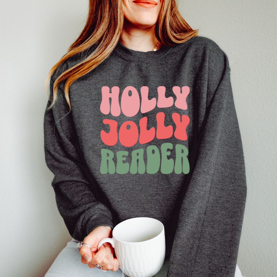 Person wearing a dark gray sweatshirt with 'Holly Jolly Reader' text, holding a white mug.